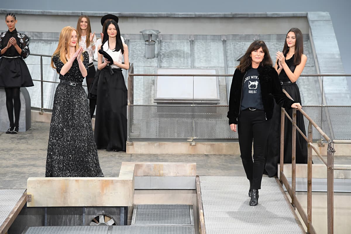 a woman walking across a bridge in a spacious room while other women watching her