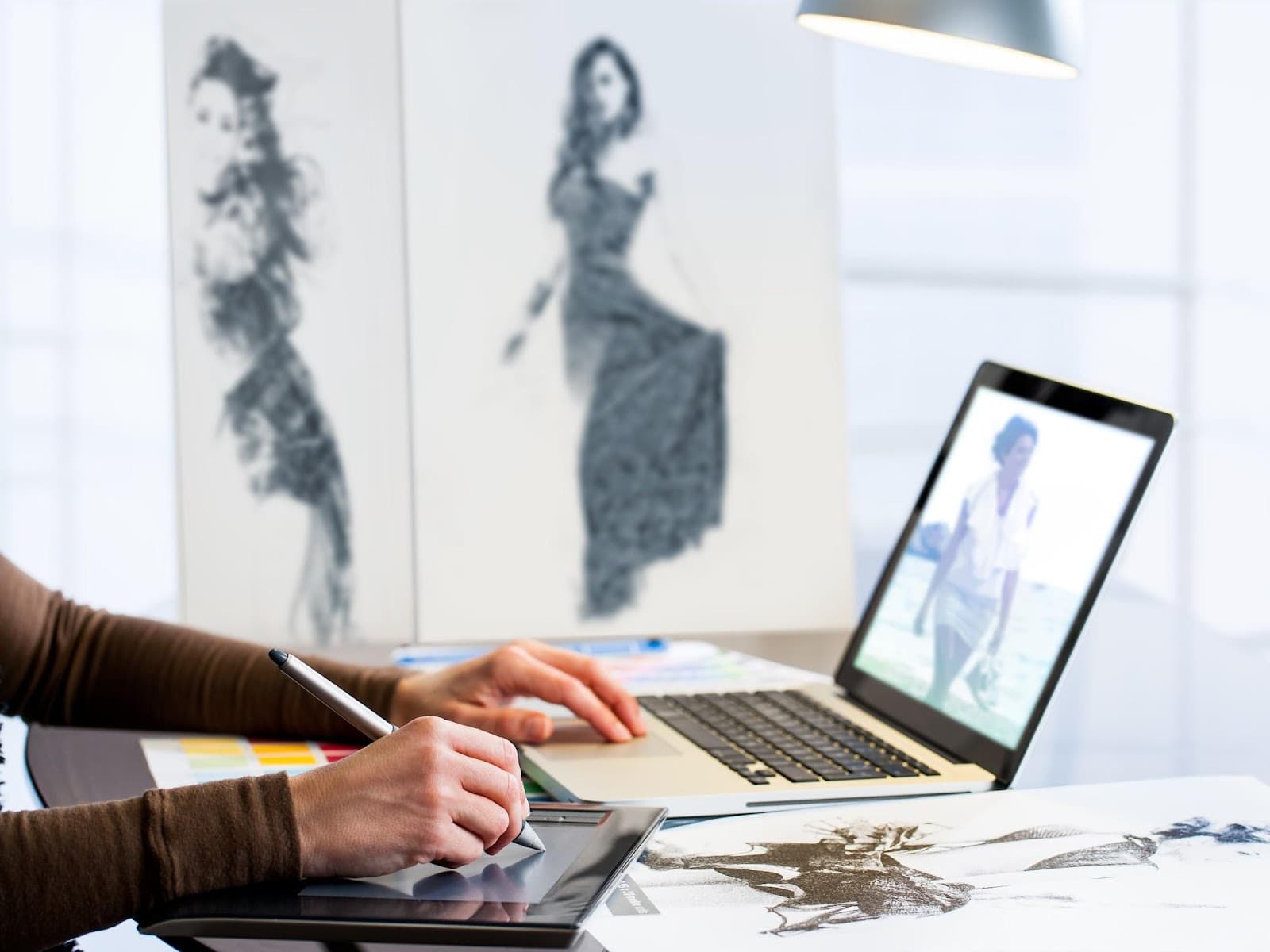 hands using a stylus on a tablet and a laptop nearby