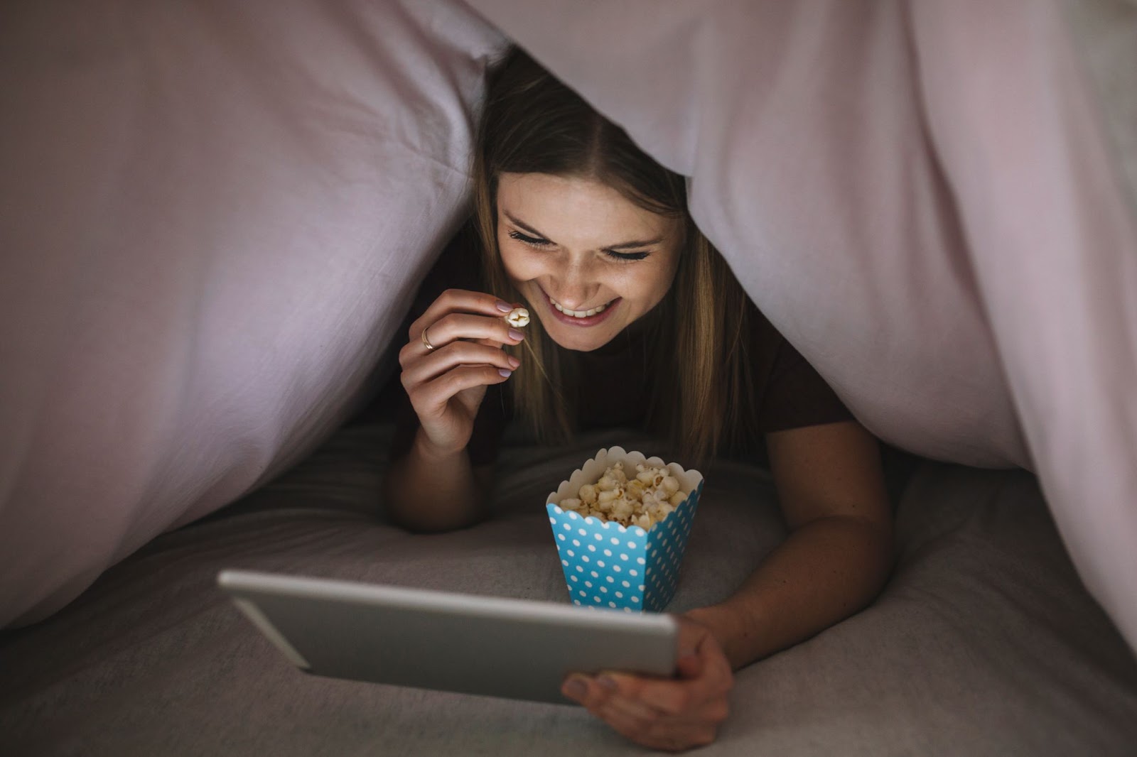 Cheerful woman watching film under the blanket
