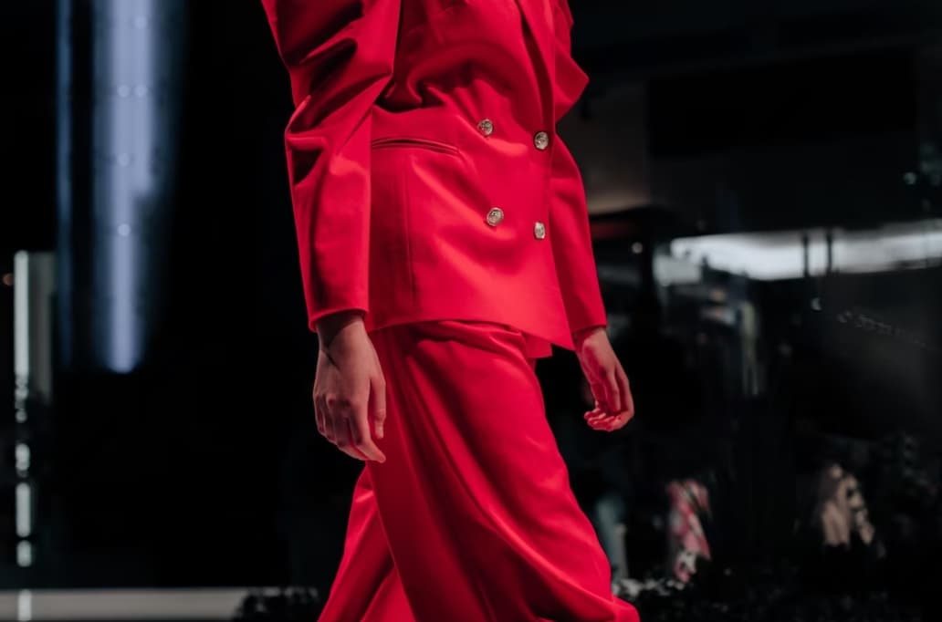 A model in a bright red suit walking on a fashion show runway