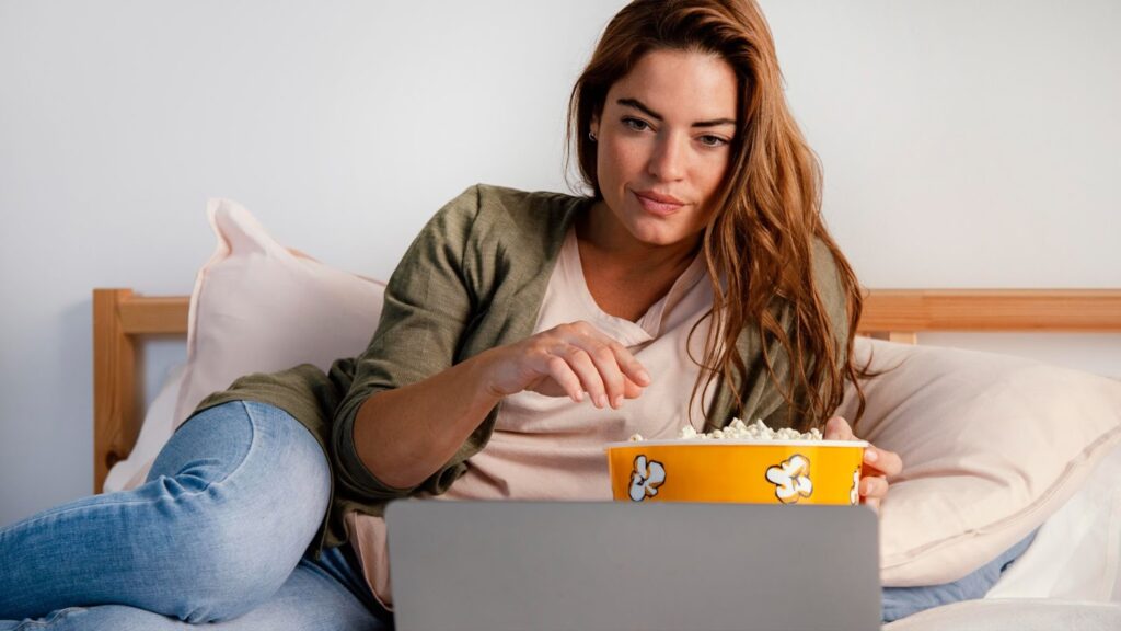Woman eating popcorn while watching movie on laptop